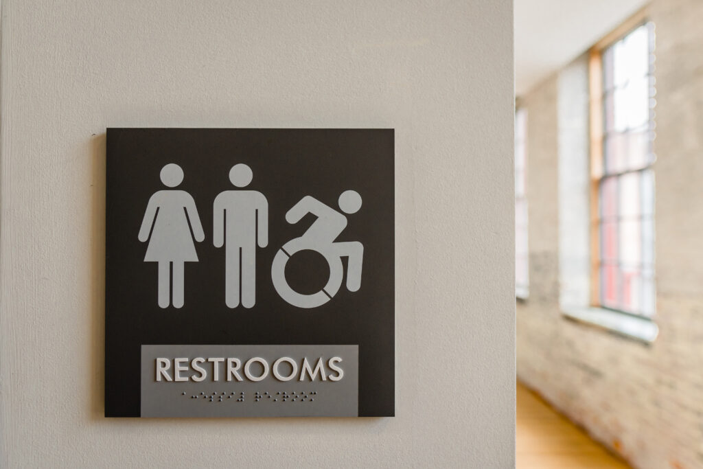 Close-up of unisex bathroom sign against neutral colored wall with symbols for male, female, and wheelchair. Copy space.